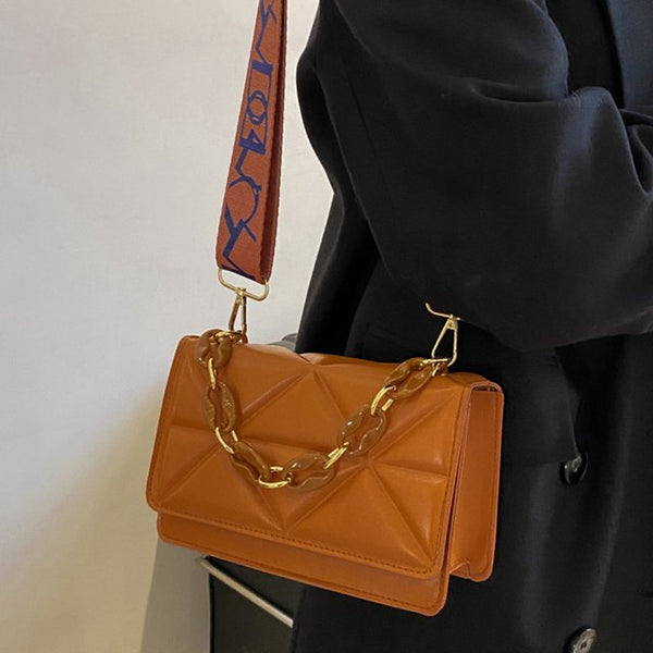 Bruine leren schoudertas met gouden ketting en verstelbare band, gedragen door persoon in zwarte jas. Stijlvolle damesaccessoire, modetrend 2023.