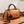 Bruine leren handtas met rozenhanger, cilindervormig ontwerp, dubbele ritsen en verstelbare schouderriem, perfect voor damesmode en accessoires.
