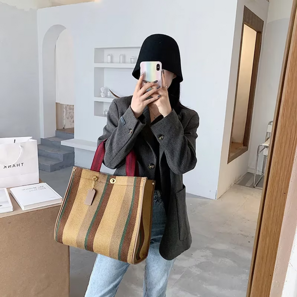 Vrouw met zwarte hoed en grijze blazer maakt selfie in moderne kamer, draagt grote gestreepte bruine tas. Mode, accessoires, binnenruimte.