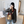 Vrouw met zwarte hoed en grijze blazer poseert met gestreepte handtas in moderne kamer. Stijlvolle mode, casual outfit, trendy accessoires.