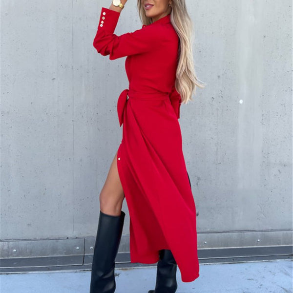 Vrouw in lange rode jurk met ceintuur en zwarte laarzen, poseert tegen een grijze muur. Modieuze dameskleding, herfststijl, elegante outfit.