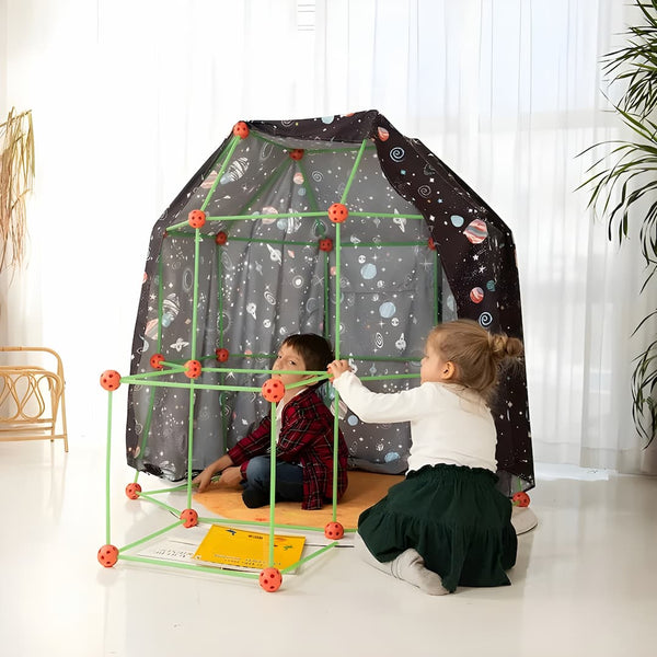 Twee kinderen spelen in een zelfgebouwd speelhuis van groene stokken en rode verbindingsstukken, bedekt met een ruimte-thema doek, in een lichte kamer.