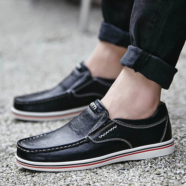Zwarte leren herenschoenen met witte stiksels en rode accenten, gedragen met opgerolde jeans. Comfortabele casual loafers voor dagelijks gebruik.