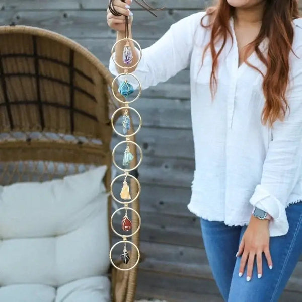 Vrouw houdt handgemaakte chakra wanddecoratie met zeven edelstenen in gouden ringen vast, boho-stijl, spirituele woondecoratie.