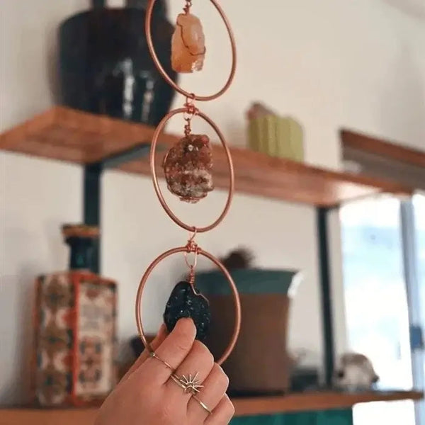 Hand houdt decoratieve chakra hanger met edelstenen in cirkels, interieurdecoratie, spirituele woonaccessoires, rustieke houten planken op achtergrond.