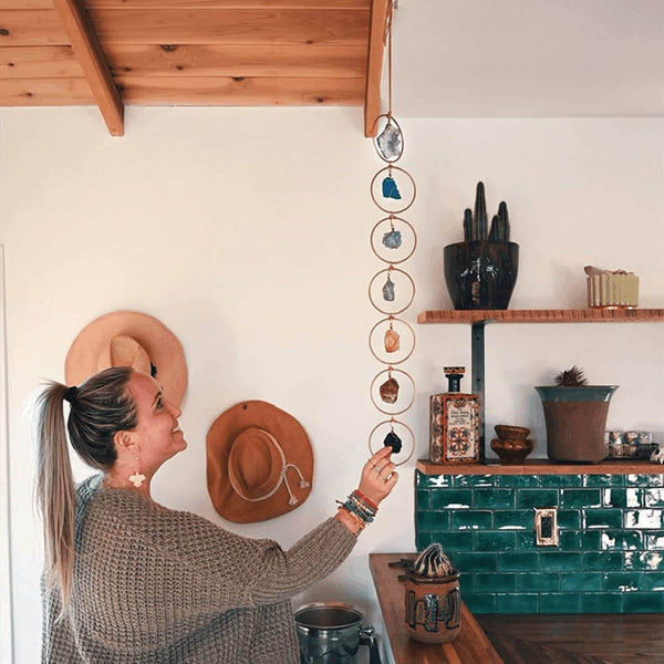 Vrouw bewondert hangende chakra decoratie met edelstenen in moderne keuken; bohemian interieur, spirituele woonaccessoires, houten plafond.