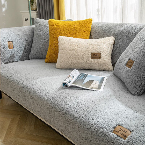 Grijze bank met ultra zachte bankhoes, gele en crèmekleurige kussens, en een open tijdschrift op houten vloer. Perfect voor moderne woonkamer.
