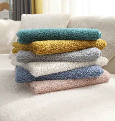 Stapel van ultra zachte bankhoezen in diverse kleuren op een crèmekleurige bank. Perfect voor interieurdecoratie en comfort.