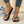 Zwarte teenslippers met vlinderdecoratie, gedragen door vrouw met witte nagellak en turquoise enkelbandje, naast een discobal en glinsterende stof.