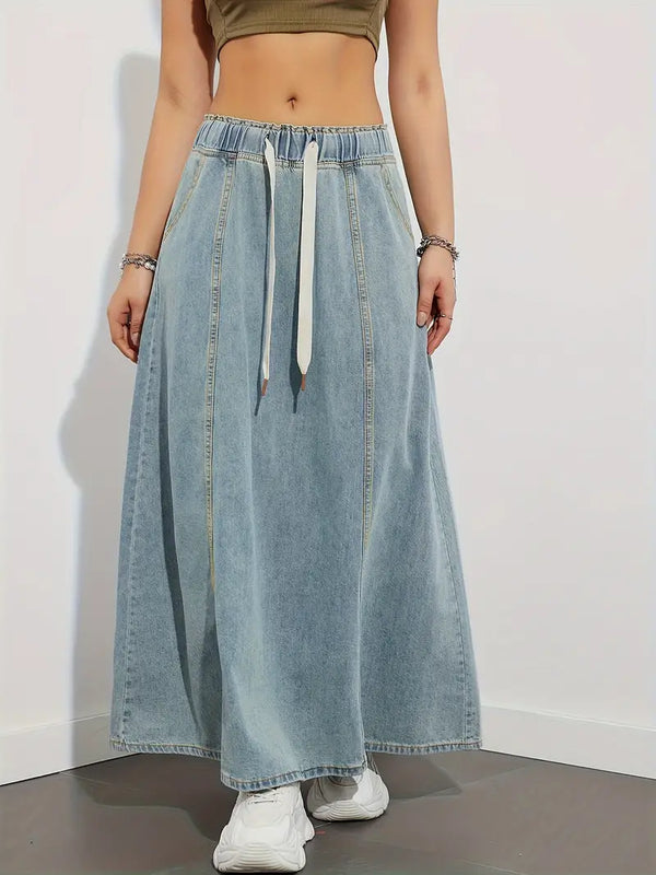 Vrouw in lange denim rok met elastische tailleband en witte veter, gecombineerd met witte sneakers. Trendy casual damesmode.