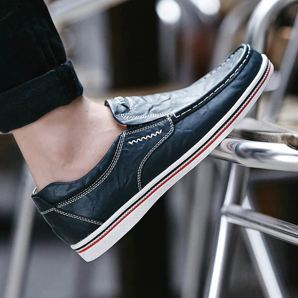 Donkerblauwe leren herenschoen met witte stiksels en rode accenten, gedragen op een metalen stoel. Stijlvolle casual loafers voor dagelijks gebruik.
