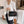 Vrouw in witte blazer met zwarte leren handtas met bloemdetail, staand in moderne kantooromgeving. Stijlvolle zakelijke mode, elegante accessoires.