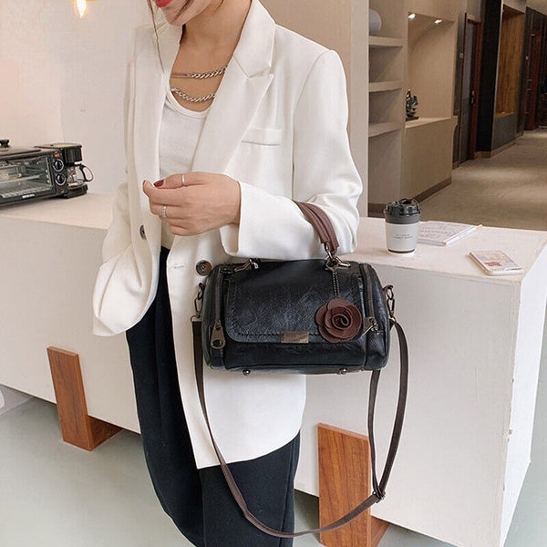 Vrouw in witte blazer met zwarte leren handtas met bloemdetail, staand in moderne kantooromgeving. Stijlvolle zakelijke mode, elegante accessoires.