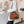 Vrouw met witte blazer draagt bruine leren handtas met roosdetail in moderne caféomgeving. Stijlvolle damesmode, trendy accessoires, casual chic.