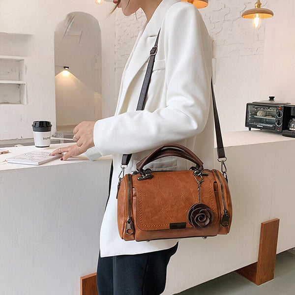 Vrouw met witte blazer draagt bruine leren handtas met roosdetail in moderne caféomgeving. Stijlvolle damesmode, trendy accessoires, casual chic.