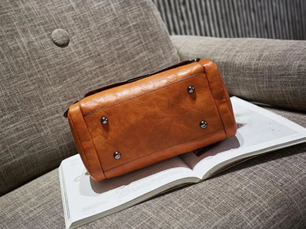 Bruine leren handtas op een open boek, liggend op een grijze stoffen stoel. Luxe damesaccessoire, stijlvolle mode, interieurdecoratie.