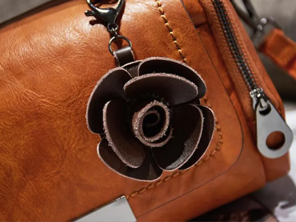Bruine leren tas met metalen rits en bloemvormige sleutelhanger. Stijlvolle damesaccessoire, perfect voor dagelijks gebruik en modieuze uitstraling.
