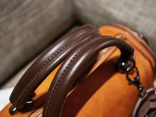 Bruine leren handtas met stevige handgrepen, stijlvolle metalen details en oranje accenten, perfect voor modieuze damesaccessoires.