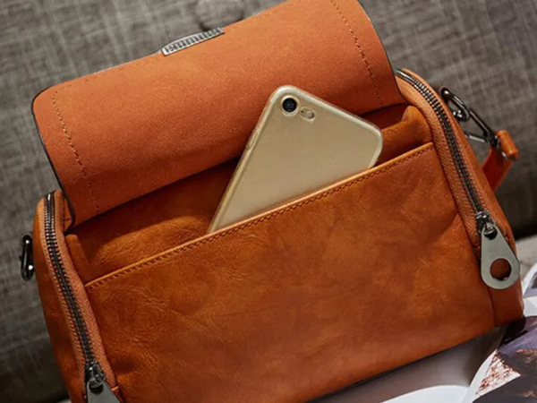 Oranje leren handtas met ritsen en een smartphone in het voorvak, stijlvolle damesaccessoire, modieuze tas voor dagelijks gebruik.