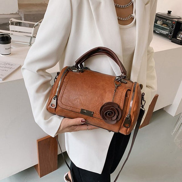 Vrouw met stijlvolle bruine leren handtas met rozenversiering, gedragen in moderne kantooromgeving. Perfecte accessoire voor zakelijke mode.