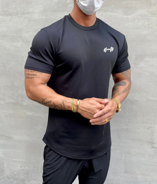 Man in zwarte sportkleding met gewichtenlogo, draagt een mondkapje. Fitness, sportkleding, gezondheid, krachttraining, tatoeages.