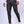 Man in grijze slim-fit broek en witte sneakers, staand tegen een neutrale achtergrond. Modieuze herenkleding, casual stijl.