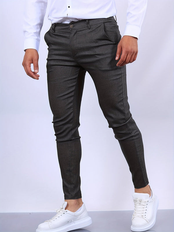 Man in grijze slim-fit broek en witte sneakers, staand tegen een neutrale achtergrond. Modieuze herenkleding, casual stijl.