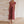 Vrouw in elegante, geplooide, roze jurk met diepe V-hals, staand tegen een stenen muur. Perfect voor avondkleding of formele evenementen.