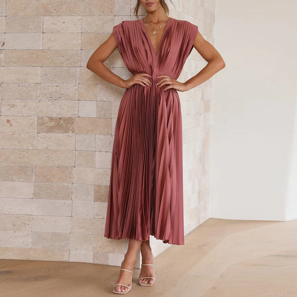 Vrouw in elegante, geplooide roze jurk met V-hals, staand tegen een stenen muur. Perfect voor avondkleding, modetrends en stijlvolle outfits.
