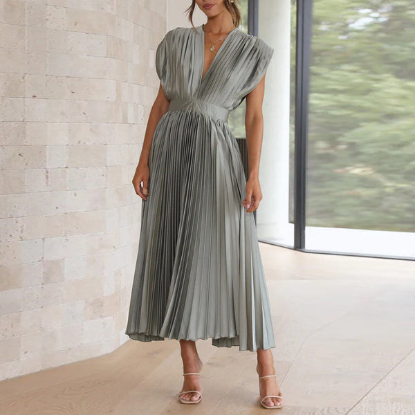 Vrouw in elegante, geplooide, zilvergrijze jurk met V-hals, staand in moderne, lichte ruimte. Perfect voor avondkleding of formele evenementen.