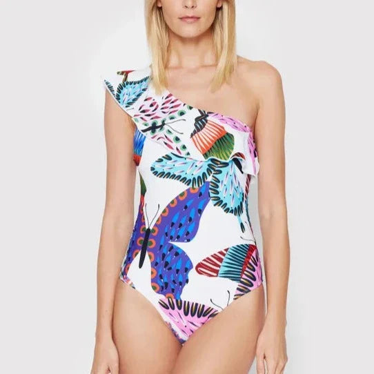 Vrouw in kleurrijk Desigual badpak met vlinderprint, asymmetrisch ontwerp, één schouderband. Perfect voor strandmode en zomertrends.