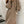 Vrouw in stijlvolle bruine trui-jurk met knopen, leunend tegen witte muur. Trendy herfstmode, comfortabele dameskleding, elegant design.