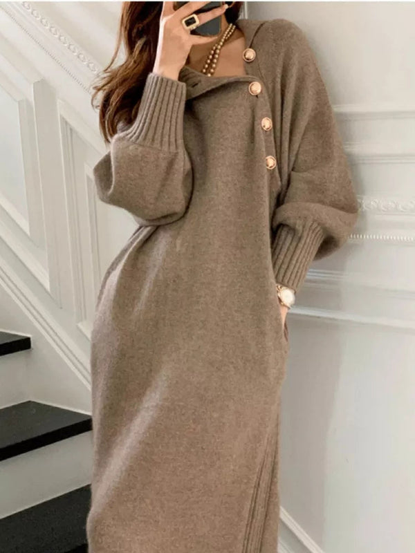 Vrouw in stijlvolle bruine trui-jurk met knopen, leunend tegen witte muur. Trendy herfstmode, comfortabele dameskleding, elegant design.