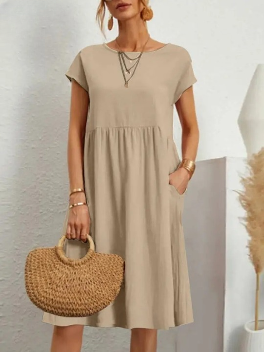 Vrouw in beige zomerjurk met korte mouwen, draagt een ronde rieten tas. Stijlvolle casual outfit, perfect voor warme dagen.