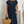 Vrouw in elegante zwarte jurk met korte mouwen, draagt een strooien handtas en gouden sieraden. Perfecte zomeroutfit voor casual en chique gelegenheden.
