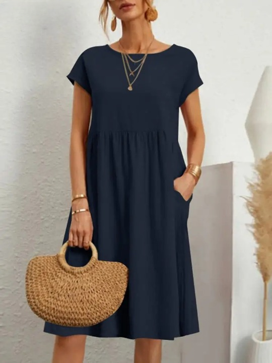 Vrouw in elegante zwarte jurk met korte mouwen, draagt een strooien handtas en gouden sieraden. Perfecte zomeroutfit voor casual en chique gelegenheden.