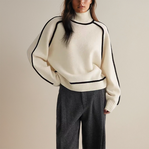 Vrouw in stijlvolle crèmekleurige trui met zwarte accenten en hoge kraag, gecombineerd met grijze broek. Modieuze dameskleding, herfst/winter stijl.