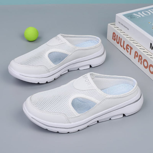 Witte ademende sportschoenen met mesh design en rubberen zool, naast een groene tennisbal en boeken op een grijze achtergrond.