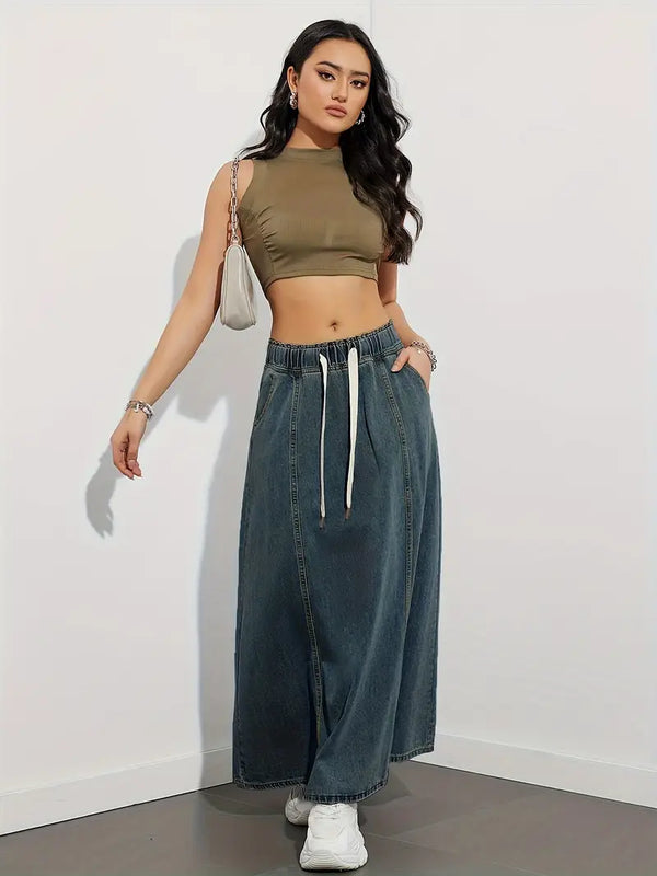 Vrouw in trendy outfit met olijfgroene crop top, lange denim rok en witte sneakers, poseert tegen witte achtergrond. Mode, casual stijl, streetwear.