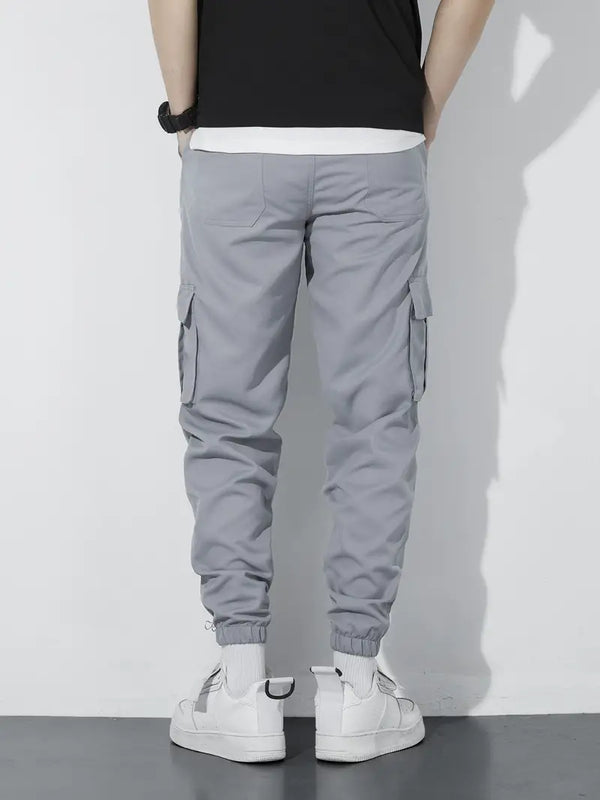 Grijze cargobroek heren, achteraanzicht, met zakken en elastische boorden, gecombineerd met witte sneakers en zwart T-shirt.