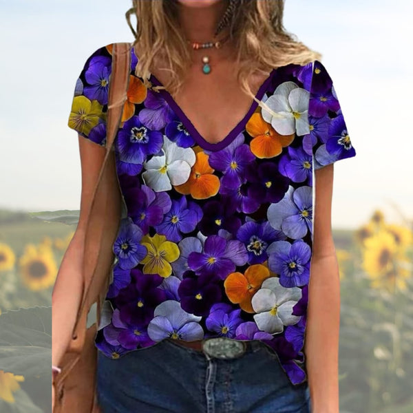 Vrouw draagt kleurrijk bloemen T-shirt met viooltjesprint, casual zomeroutfit, modetrend, buiten in zonnebloemveld.
