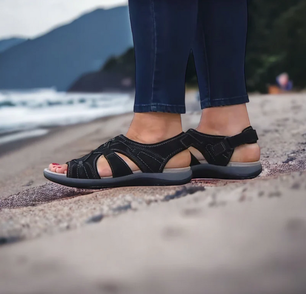 Zwarte sandalen voor dames op een zandstrand, comfortabele zomerschoenen, ideaal voor wandelen langs de kustlijn, modieuze en duurzame sandalen.