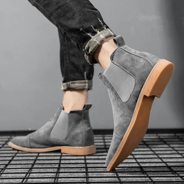 Grijze suède Chelsea boots voor heren, met elastische zijkanten en bruine zool, gedragen met opgerolde zwarte jeans. Stijlvolle herenschoenen.