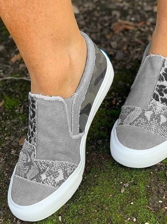 Grijze canvas instappers met dierenprint en camouflage-accenten, gedragen op mosrijke ondergrond. Trendy damesschoenen, casual stijl.