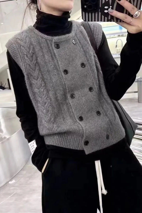 Grijze gebreide damestrui met kabelpatroon en dubbele rij knopen, gedragen over een zwarte coltrui. Modieuze winterkleding, casual stijl.