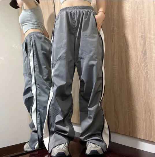 Grijze trainingsbroek met witte strepen, gedragen door persoon voor spiegel. Sportieve mode, comfortabele pasvorm, trendy streetwear-stijl.