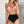 Vrouw in roze bikini top en zwarte hoge taille bikini broekje poseert tegen witte bakstenen muur. Zomermode, strandkleding, dames badmode.