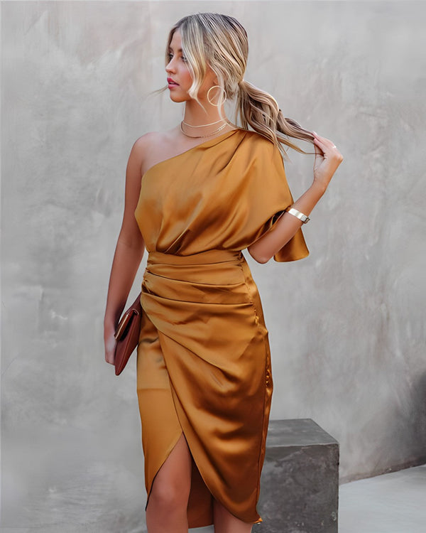 Vrouw in elegante, goudkleurige asymmetrische satijnen jurk, poseert tegen een neutrale achtergrond. Trendy mode, avondkleding, chique stijl.