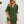 Vrouw in groene zomerjurk met driekwart mouwen, draagt zonnebril en witte handtas. Modieuze dameskleding, casual stijl, trendy outfit.