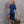 Vrouw in elegante blauwe satijnen jurk met asymmetrische schouder, beige sandalen en bruine handtas. Modieuze outfit, stedelijke achtergrond.